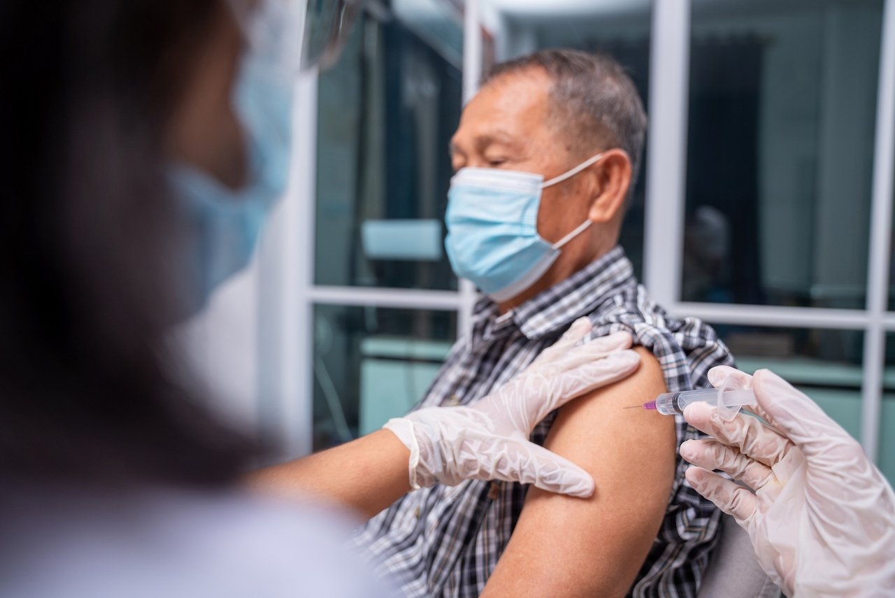 一名灰白头发的男子戴着口罩，正在左臂上注射疫苗