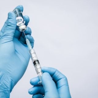 A doctor wearing blue gloves uses a small syringe to extract immunotherapy from a vial